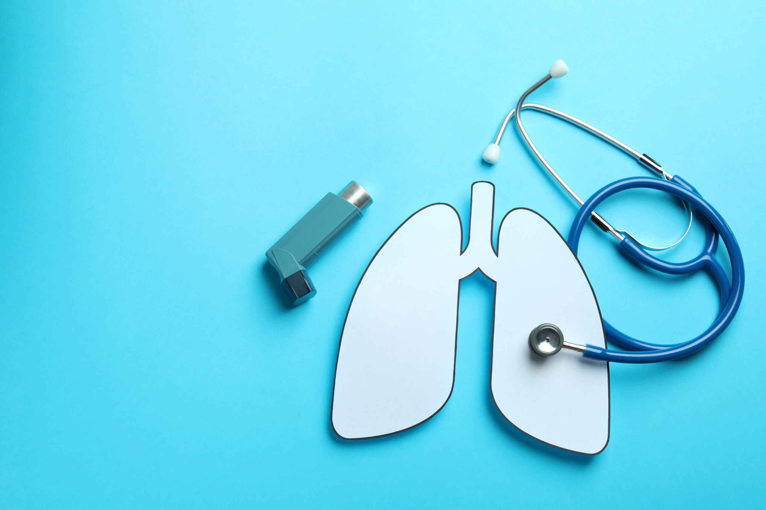 Decorative lungs, stethoscope and inhaler on blue background